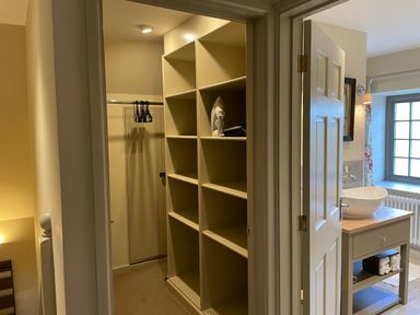 A walk-in closet with shelves and an iron next to a bathroom with a sink and window at Omas Cottage in Moreton-In-Marsh