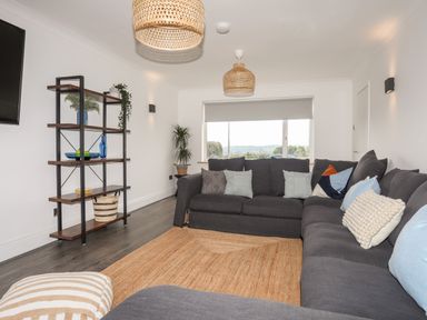 A living room with a large gray sectional sofa and pillows a wooden shelf with plants and decor and a window with a blind at Dolwyn in Llandegfan