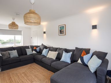 A living room with a large dark gray sectional sofa with multiple cushions and woven pendant lights at Dolwyn in Llandegfan