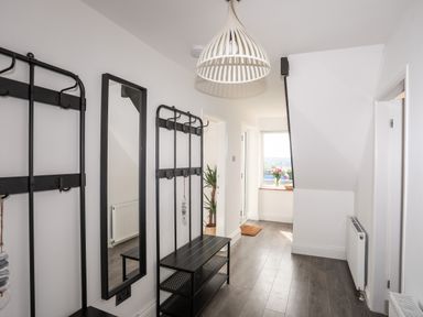 A hallway with a black bench and wall-mounted coat racks a mirror a window with flowers and a wooden floor at Dolwyn in Llandegfan
