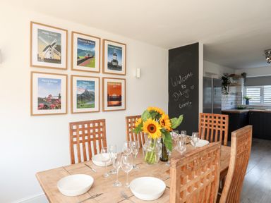 A dining area with a wooden table set with plates and glasses sunflowers in a vase and wall art in Dolwyn Llandegfan