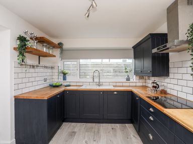 A kitchen with black cabinets wooden countertops white subway tile backsplash and a window above the sink at Dolwyn in Llandegfan