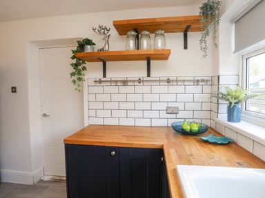 A kitchen corner with wooden countertops black cabinets white tiled backsplash and floating shelves at Dolwyn in Llandegfan