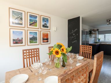 A dining area with a wooden table and chairs set with plates and glasses a vase of sunflowers on the table and framed pictures on the wall at Dolwyn in Llandegfan
