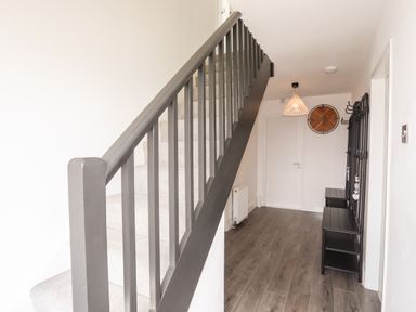 A hallway with a staircase a clock a hanging light and black benches at Dolwyn in Llandegfan
