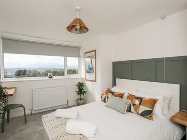A bedroom with a bed with colorful pillows and towels near a window with a roller blind at Dolwyn in Llandegfan