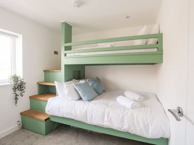 A bedroom with a green bunk bed and stairs near a window at Dolwyn in Llandegfan