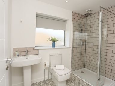 A bathroom with a pedestal sink a toilet and a walk in shower with patterned floor tiles at Dolwyn in Llandegfan