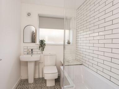A bathroom with a sink mirror toilet bathtub and tiled walls at Dolwyn in Llandegfan