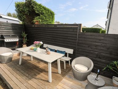 An outdoor patio with a table, bench, wicker chairs, a barbecue grill, and potted plants at Dolwyn in Llandegfan