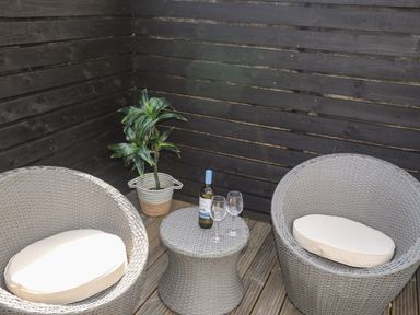 A corner patio with two round wicker chairs and a small wicker table with a bottle and two glasses at Dolwyn in Llandegfan