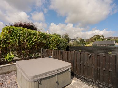 A hot tub with a cover in a small fenced garden with hedges and a shed at Dolwyn in Llandegfan