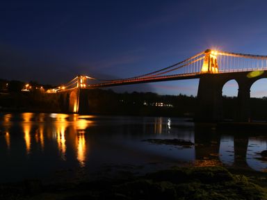 A suspension bridge illuminated at night over a body of water at Dolwyn in Llandegfan