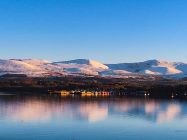 A body of water with boats docked and snow-covered mountains in the background at Dolwyn in Llandegfan