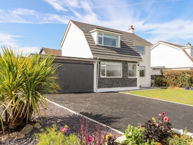 A detached house with a gray roof a double garage a driveway plants and flowers in the garden at Dolwyn in Llandegfan