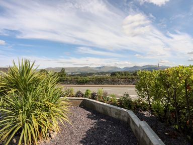 A garden with plants a stone wall and mountains in the background at Dolwyn in Llandegfan
