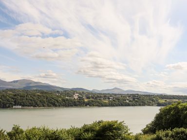 A river with trees on both sides and hills in the background under a cloudy sky at Dolwyn in Llandegfan