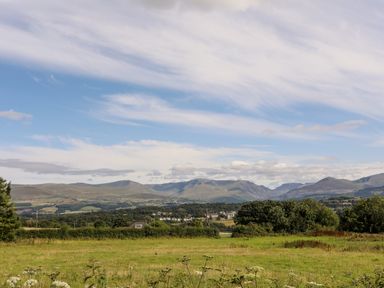 A rural landscape with fields trees and distant hills under a partly cloudy sky at Dolwyn in Llandegfan