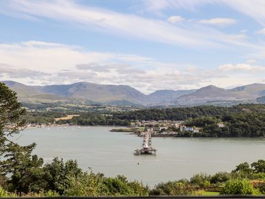 A view of a pier extending into a body of water with a town and mountains in the background at Dolwyn in Llandegfan