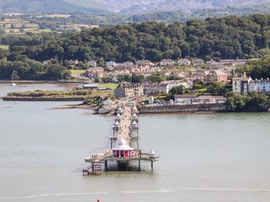A pier extending into water with buildings and trees in the background at Dolwyn in Llandegfan