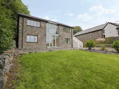 A stone house with multiple windows and a green lawn in front at Tan Twr in Llanfairpwll