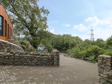 A paved driveway with stone walls and trees near a wooden building at Tan Twr in Llanfairpwll