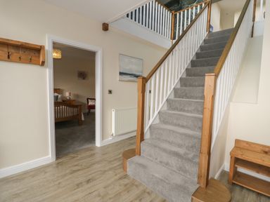 A hallway with carpeted stairs wooden banisters a wooden bench and a coat rack at Tan Twr in Llanfairpwll