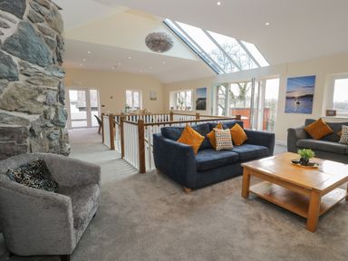 A living room with sofas a coffee table and a stone wall next to large skylights at Tan Twr in Llanfairpwll
