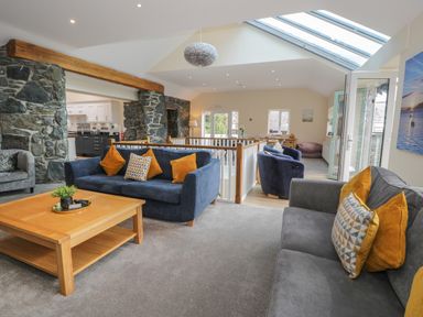 A living room with sofas and a wooden coffee table next to a stone wall and open kitchen at Tan Twr in Llanfairpwll