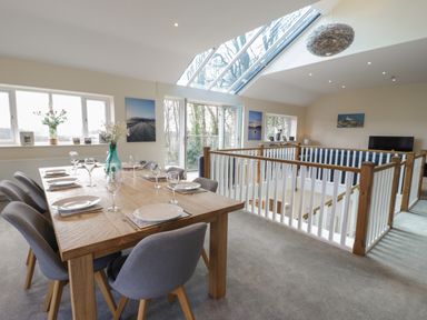 A dining area with a wooden table set for eight and chairs near large windows and a skylight at Tan Twr in Llanfairpwll
