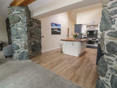 A kitchen with a wooden island and stools next to stone wall pillars at Tan Twr in Llanfairpwll