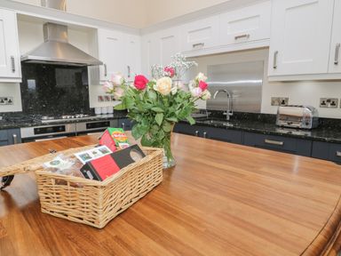 A kitchen with a wooden island counter a basket of food items a vase with flowers a stovetop a sink and a toaster at Tan Twr in Llanfairpwll