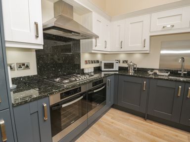 A kitchen with dark lower cabinets and white upper cabinets with a stove microwave kettle and sink at Tan Twr in Llanfairpwll