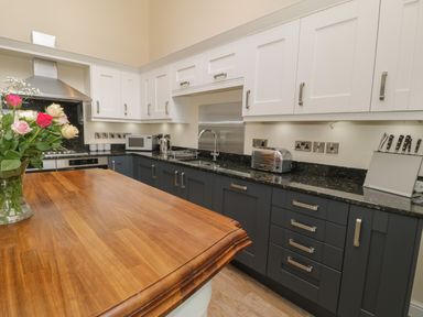 A kitchen with wooden countertop flowers in a vase white and dark cabinets toaster microwave and a knife block at Tan Twr in Llanfairpwll