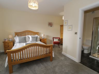 A bedroom with a wooden bed, bedside tables with lamps, a red chair, wooden wardrobe, and an attached bathroom at Tan Twr in Llanfairpwll