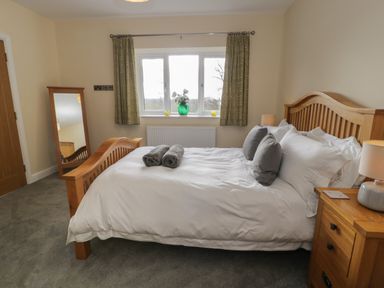 A bedroom with a wooden bed and bedside table a window with curtains and a full length mirror at Tan Twr in Llanfairpwll