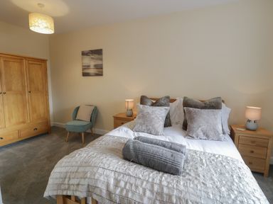 A bedroom with a double bed with pillows and blankets two wooden bedside tables with lamps a wooden wardrobe a chair and a wall picture at Tan Twr in Llanfairpwll