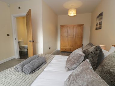 A bedroom with a bed holding rolled towels and cushions a wooden wardrobe an open door showing a bathroom at Tan Twr in Llanfairpwll