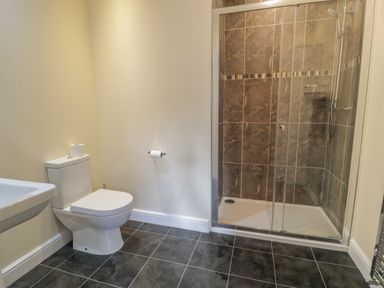 A bathroom with a toilet a shower with glass doors and tiled walls and floor at Tan Twr in Llanfairpwll