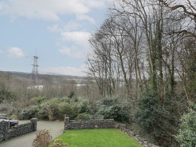An outdoor scene with a stone wall, green grass, leafless trees and a power line tower at Tan Twr in Llanfairpwll