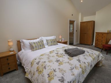 A bedroom with a bed with floral bedspread and pillows two bedside tables with lamps a wardrobe a chest of drawers and a red chair at Tan Twr in Llanfairpwll