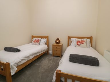 A bedroom with two single beds white bedding and crab pillows with a nightstand and lamp between the beds at Tan Twr in Llanfairpwll