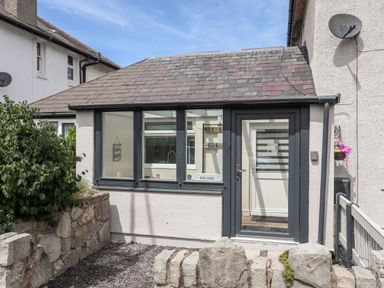 Small stone and slate roof house with glass door and windows and a low stone wall at Beeches Bach in Prestatyn