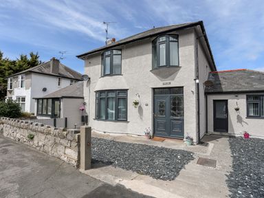 A two story house with bay windows and a stone wall at Beeches Bach in Prestatyn