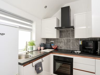 A kitchen with a white fridge sink pink mugs oven and microwave at Beeches Bach in Prestatyn