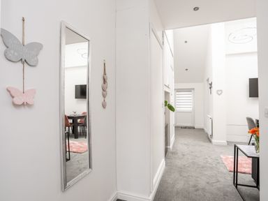A hallway with a wall mirror butterflies wall decor gray carpet and a dining table visible at Beeches Bach in Prestatyn