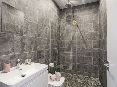 A bathroom with a white sink, toilet, and walk-in shower with pebble flooring at Beeches Bach in Prestatyn