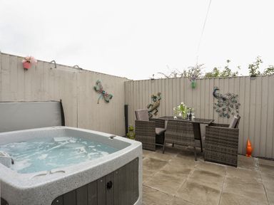 An outdoor patio with a hot tub a dining table with chairs and decorative wall art at Beeches Bach in Prestatyn