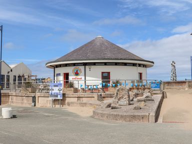 A round building with a sign for handmade ice cream red boat next to a stone monument and sand at Beeches Bach in Prestatyn