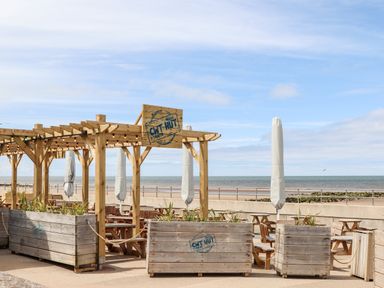 An outdoor seating area with wooden tables and planters by the sea at Beeches Bach in Prestatyn